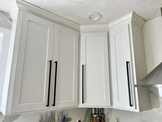 White maple kitchen cabinets with black handles, custom shaker style doors, porcelain marble look backsplash, recessed lighting, and a knife block on the countertop.