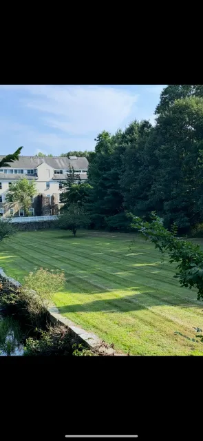 A large grassy field with trees in the background and a house in the background.