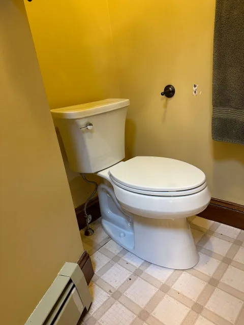 Toilet in bathroom with yellow walls, towel, and patterned floor.