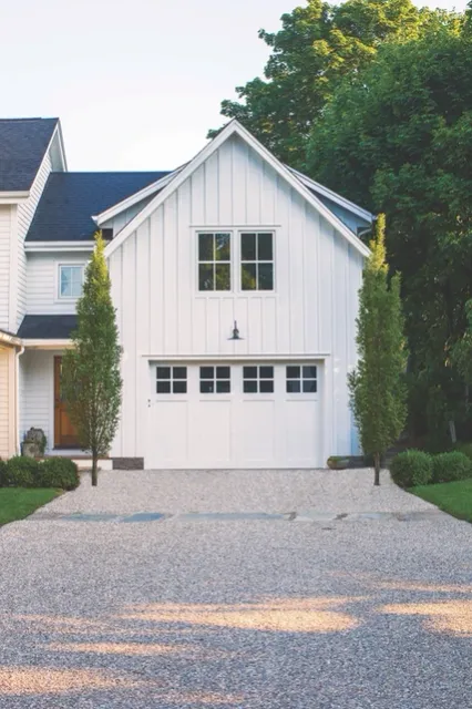 A modern white home with a two-car garage, a gravel driveway, and a small porch overhang.