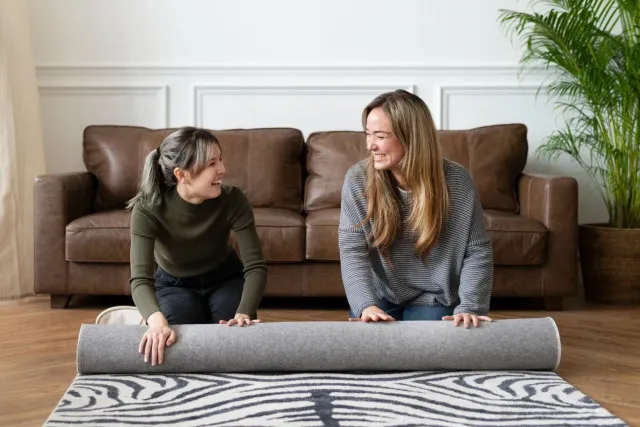 Two women are sitting on the floor looking at a rug.