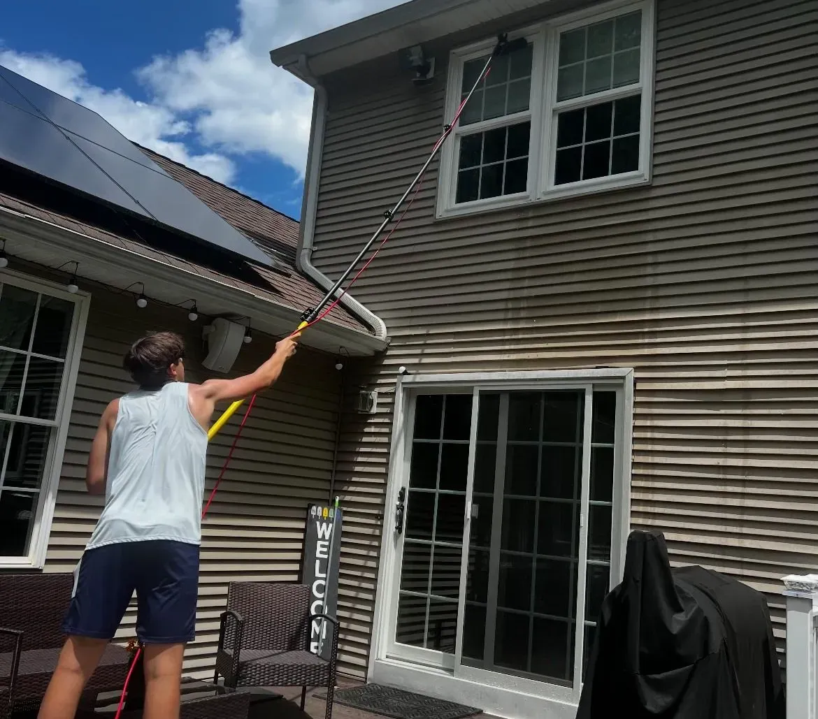 Josh Drumm cleaning a home's gutters and exterior with a water-fed pole in Southwick, MA