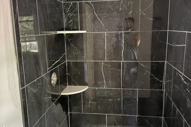 Black marble-look large-format shower with corner shelves and a low-profile base by Dmtilellc in Berlin, CT
