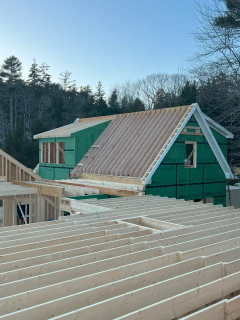 Exposed wooden roof trusses and rafters being installed over a home wrapped in green ZIP System sheathing.