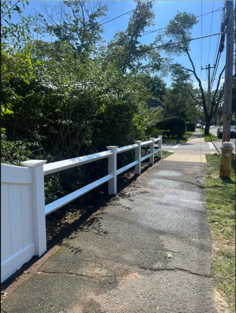 A white fence along a sidewalk next to a road.