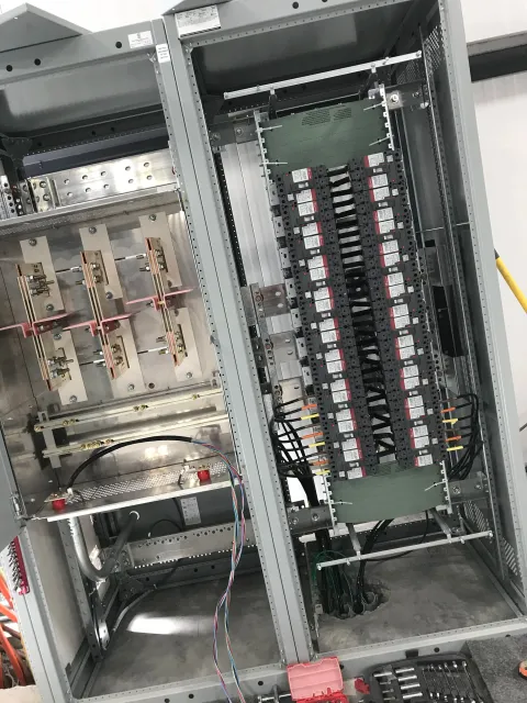 Open electrical panel with circuit breakers and wiring inside a metal enclosure, with some components mounted and wires connected.