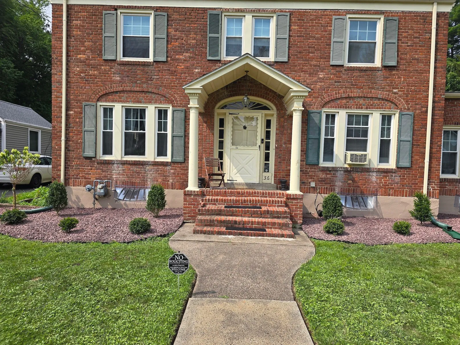 Red brick house with a cream-colored front door and porch. A walkway leads from the grassy lawn to the front entrance.