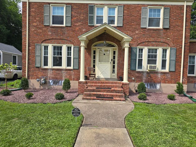 Red brick house with a cream-colored front door and porch. A walkway leads from the grassy lawn to the front entrance.