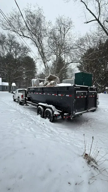 White pickup truck towing a black trailer filled with debris, parked on a snow-covered road.