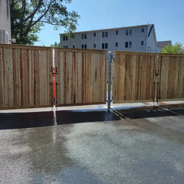 Wooden fence with a gate, in a paved area, under a bright blue sky.