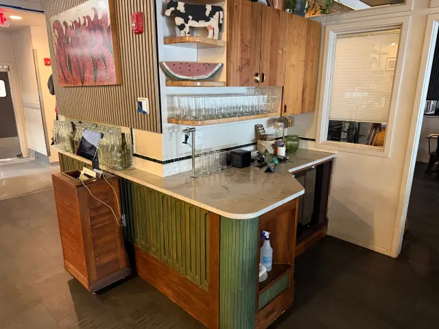 Wood-paneled café counter with sink, coffee machine, and white door in the background.