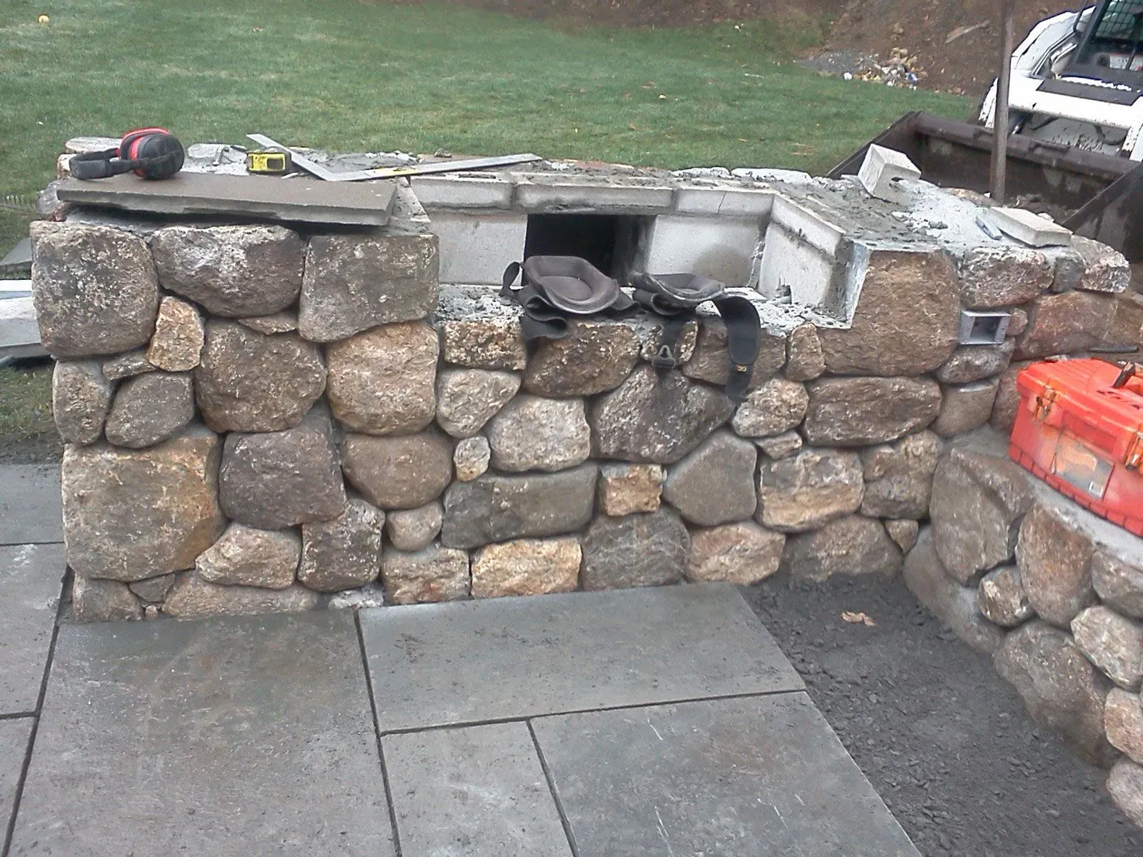 Stone outdoor wall with a flat cap, built-in fire pit opening, and paving stones in front