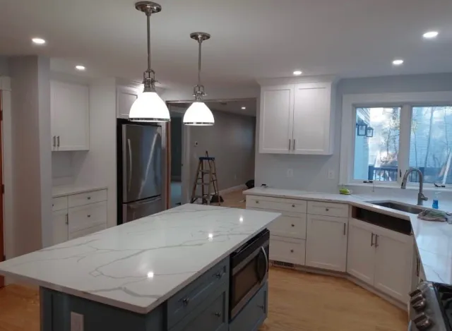 Kitchen with white cabinets, a marble countertop island, stainless steel refrigerator, and large window with a view outside.