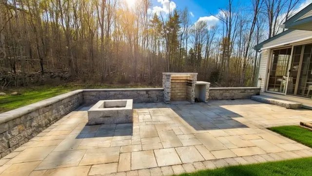 Large paver patio with square fire pit and stone retaining wall in Concord, NH