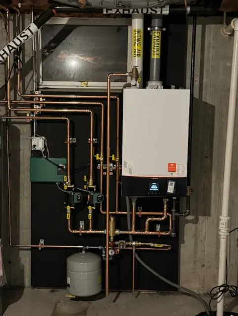 Copper pipe and boiler system in a basement setting, with black insulation, ventilation, and a water tank.