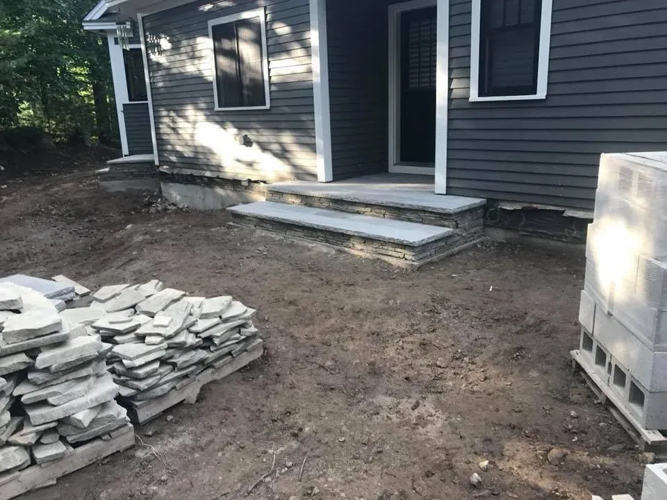 Construction site with stone steps leading up to a house entrance, and building materials stacked nearby.