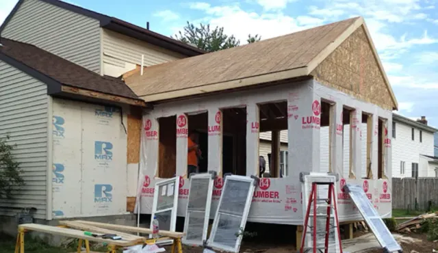 House under construction with white siding, exposed insulation, and ladders in front