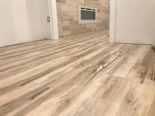 Light wood-look flooring extends into a room with a light wood-paneled wall and white doors.