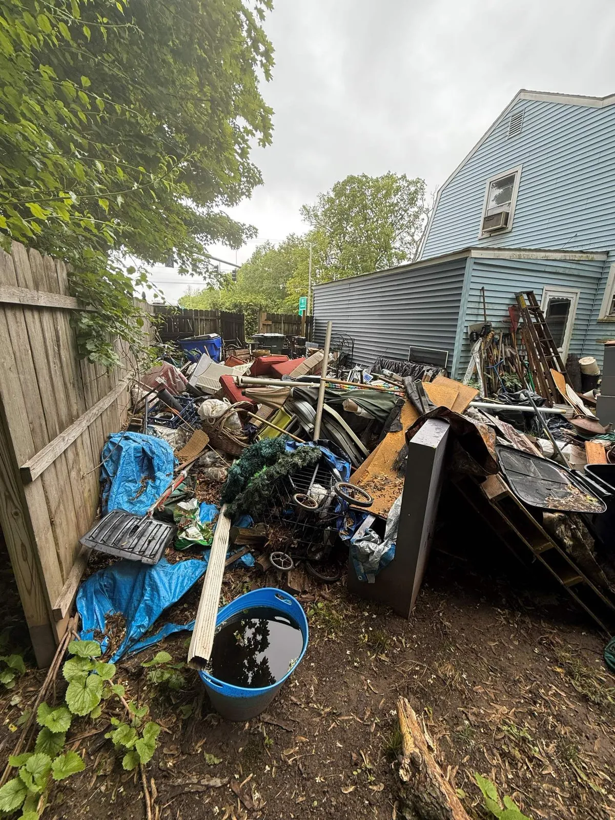 Backyard cluttered with debris; blue house in the background, cloudy sky.