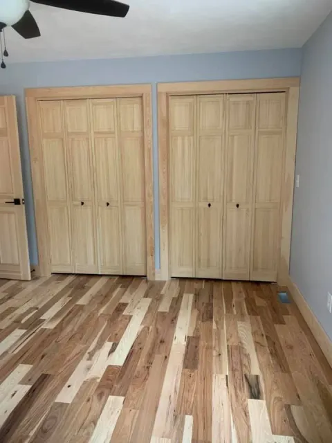 A bedroom with hardwood floors , closets , and a ceiling fan.