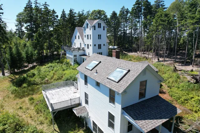 Two white houses with decks and skylights among trees