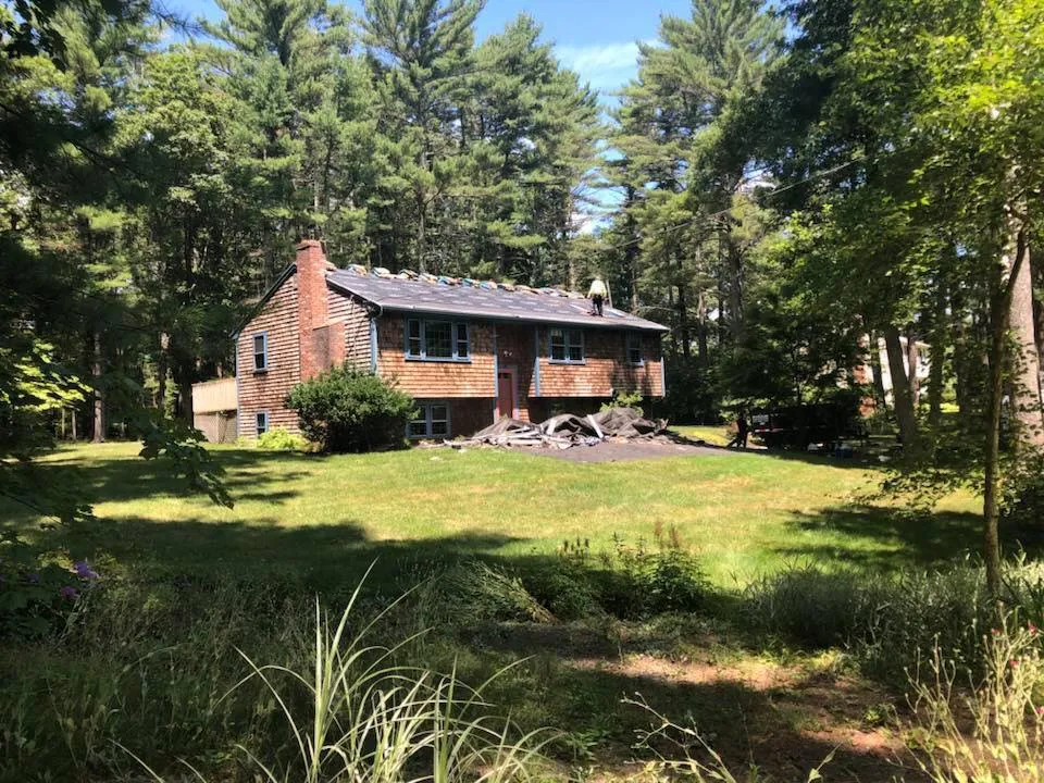 Cedar-shingle South Shore MA home undergoing a roof replacement with a Jennifer Construction roofer working on the roof