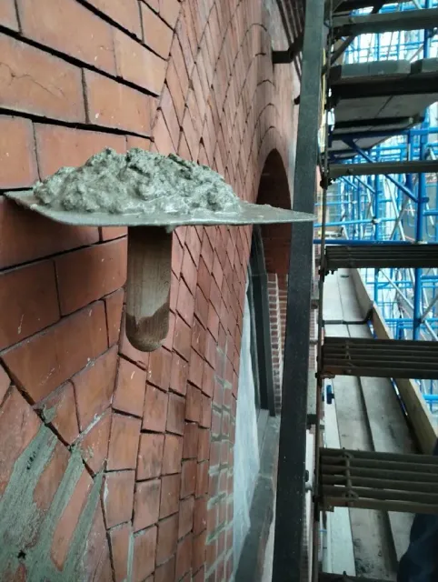A man is standing on a scaffolding cleaning a brick wall