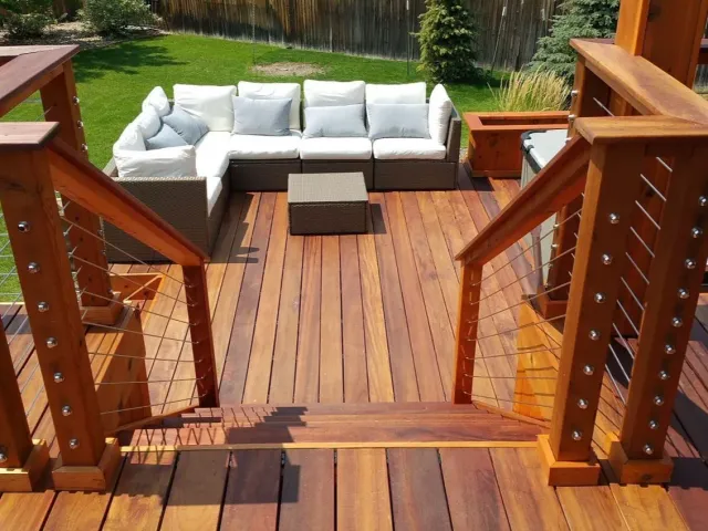 Wooden deck with stairs, a sectional sofa, and a coffee table in a backyard.