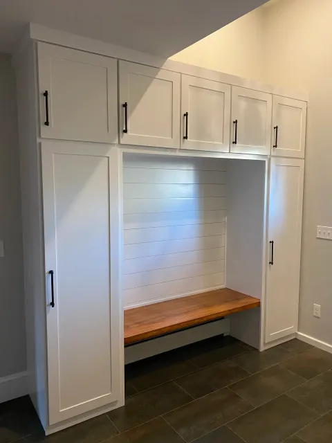 Custom built-in storage with white cabinets, shiplap wall, and wood bench