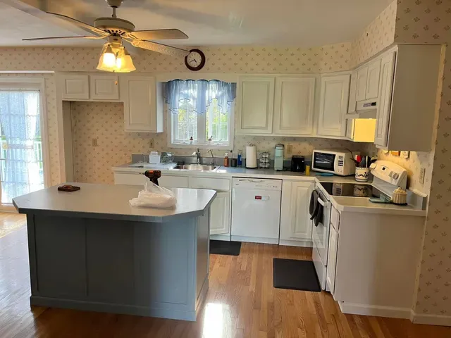 A kitchen featuring white cabinets, a gray island, light wood floors, and patterned wallpaper.