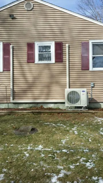 Tan house exterior with red shutters. Air conditioning unit on the ground, beige. Partially snow-covered lawn.