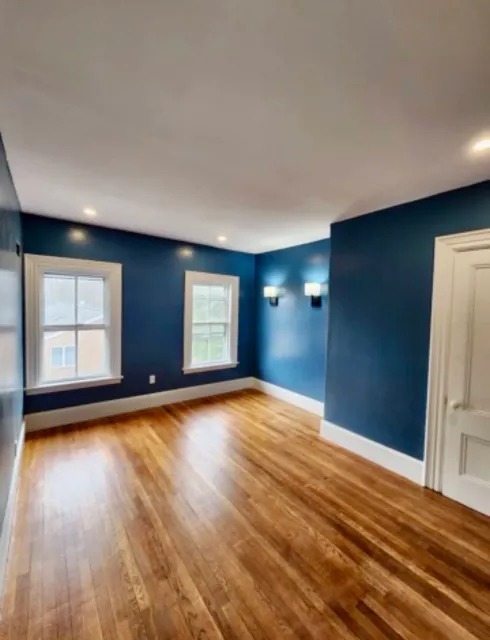 Blue room with recessed ceiling lights, two wall sconces, white trim and wood flooring.