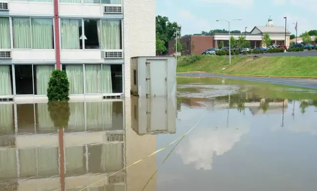 Flooded parking area beside a building, with water reflecting the facade and nearby houses.