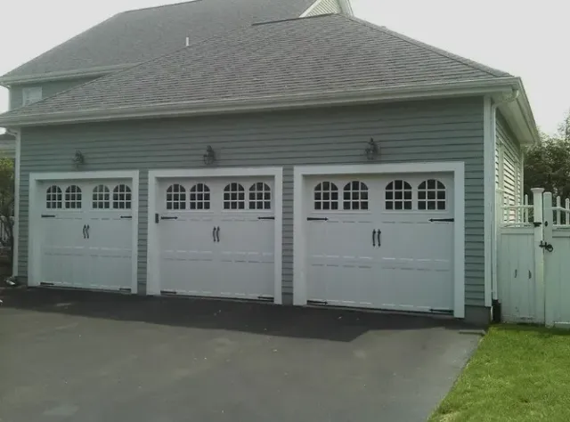 Three-car garage with white doors, gray siding, and a dark asphalt driveway.