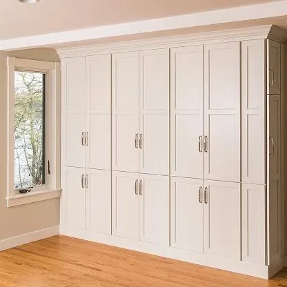 Built-in white bedroom cabinets with silver handles beside a window and hardwood floor