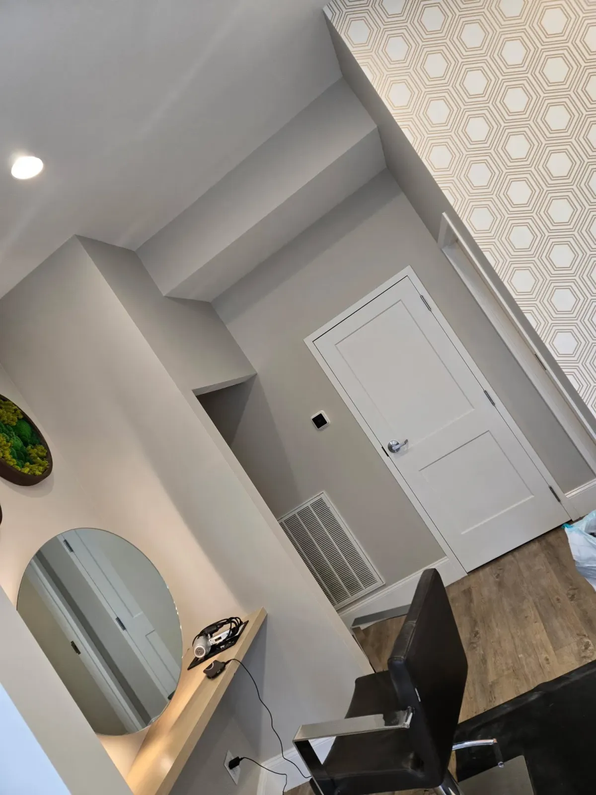 Modern room with white door, wood floor, black chair, mirror, and patterned curtain.