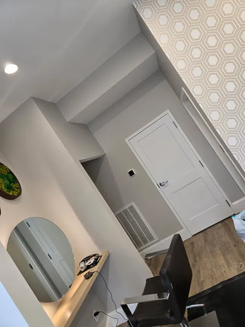 Modern room with white door, wood floor, black chair, mirror, and patterned curtain.