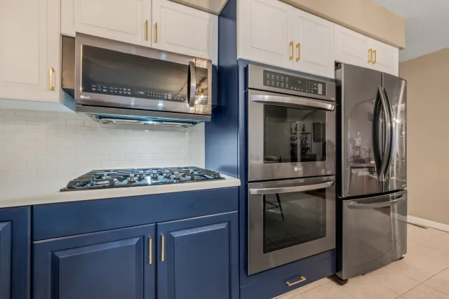 Modern kitchen featuring blue lower cabinets, white upper cabinets, stainless steel appliances, and a gas stovetop.