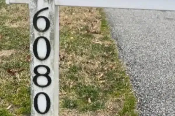 Before: Address sign with the number 6080 displayed prominently on a post beside a grassy area and a gravel path.