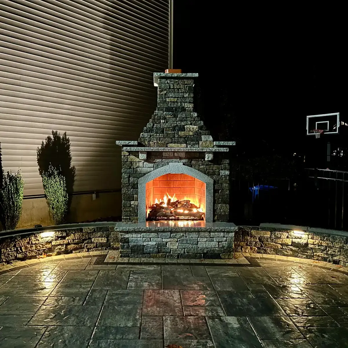 Outdoor gas burning fireplace with granite sitting walls off of a paver patio