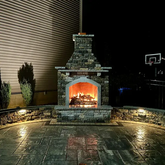 Outdoor gas burning fireplace with granite sitting walls off of a paver patio