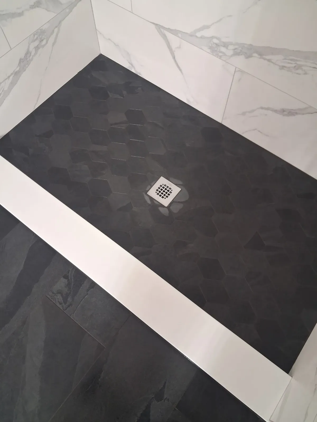 Black tiled corner with a small square drain cover on the floor.
