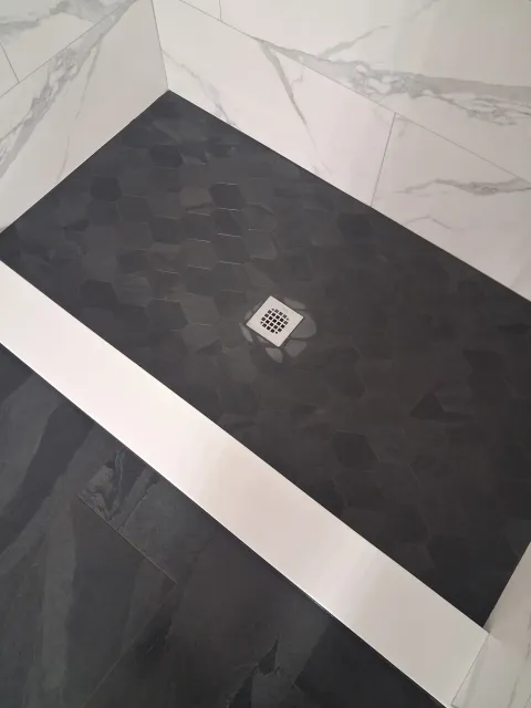 Black tiled corner with a small square drain cover on the floor.
