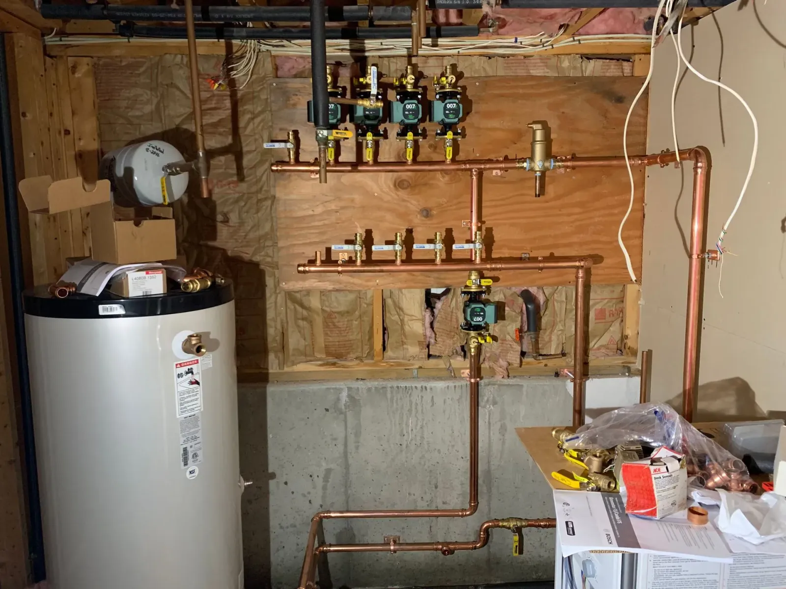 Basement utility wall with water heater, pipes, valves, and exposed framing