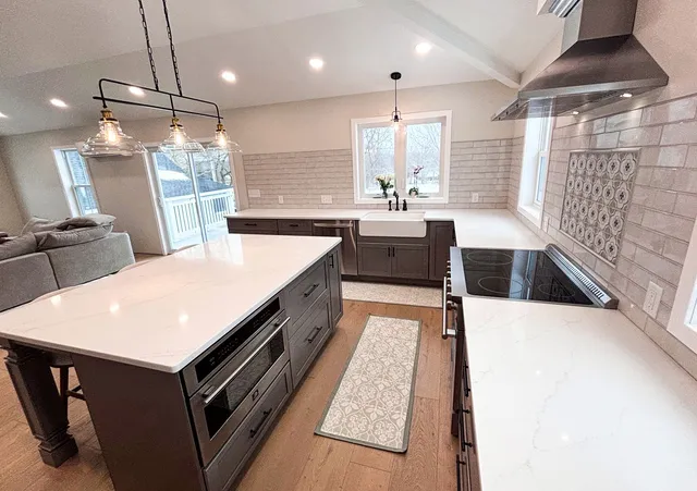 Bright modern kitchen with white island, wood floors, large window, and stainless steel range hood.