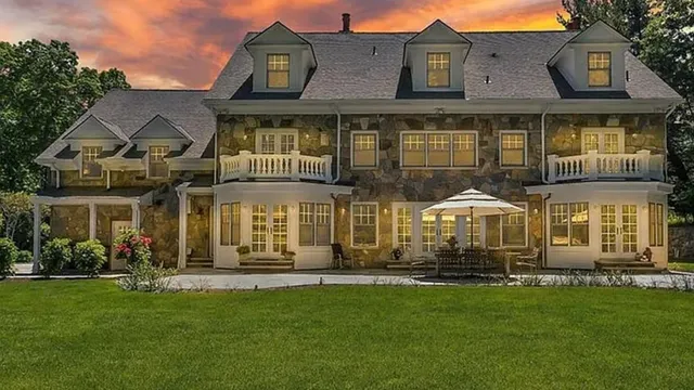 Stone and shingle home at dusk with warm lights, built by Ariola Building Contractor