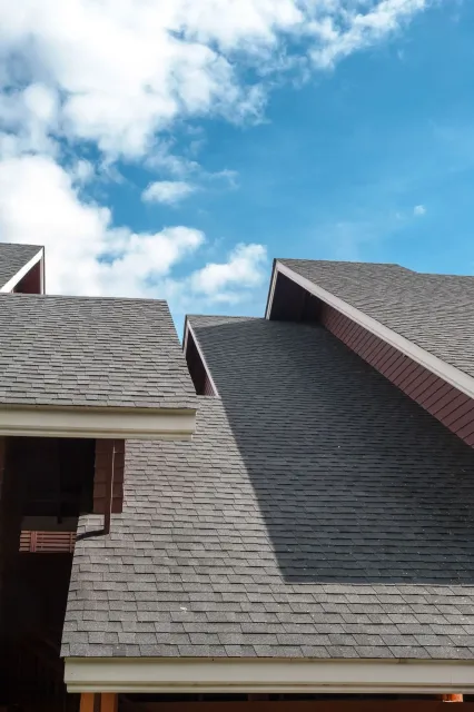 Dark gray shingled roofs against a bright blue sky with white clouds.