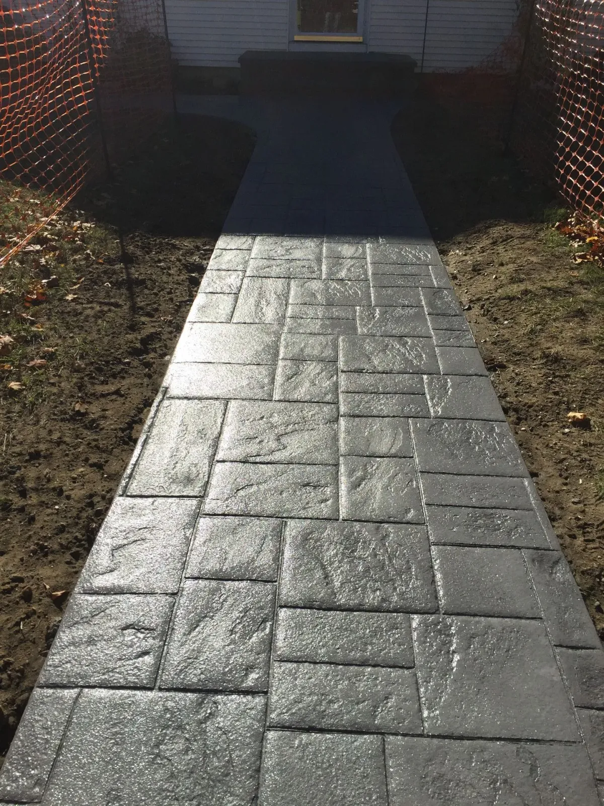 A concrete walkway leading to a house with a fence in the background.
