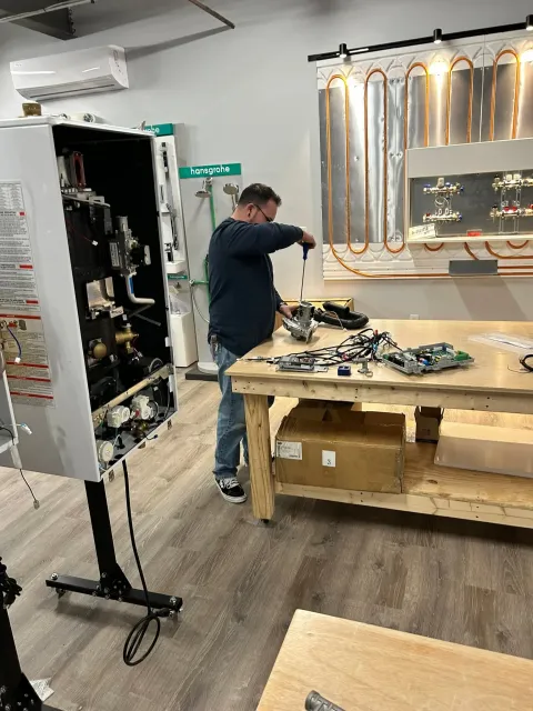 Person working at a cluttered electronics workbench in a lab with mounted cables and equipment.