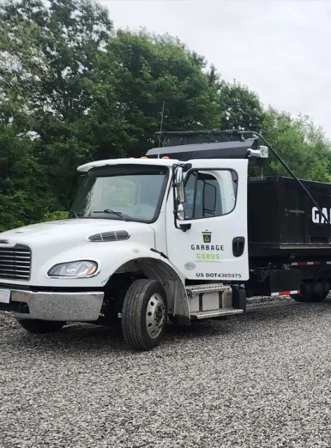Garbage Gurus junk removal truck parked beside a black dumpster, surrounded by greenery, showcasing eco-friendly waste disposal services.